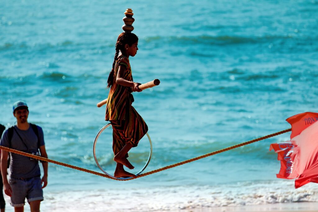 Young girl performing a rope-walking act with pots on her head at a beach.