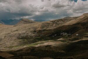 Remote Himalayan village surrounded by barren rocky mountains and lush green farmland.