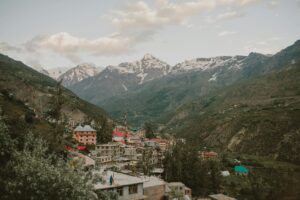 Colorful town of Manali nestled in green mountains with snow-covered peaks in the background, perfect June destination in India.