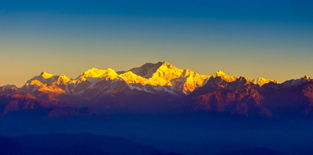 A breathtaking sunrise view from Tiger Hill, showcasing snow-capped Himalayan peaks bathed in golden light against a clear blue sky.