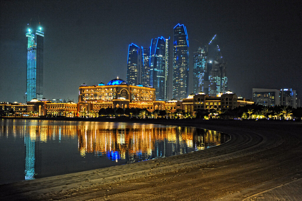 A captivating night view of the Abu Dhabi skyline featuring the illuminated Emirates Palace and modern skyscrapers, reflected beautifully in the calm waterfront.