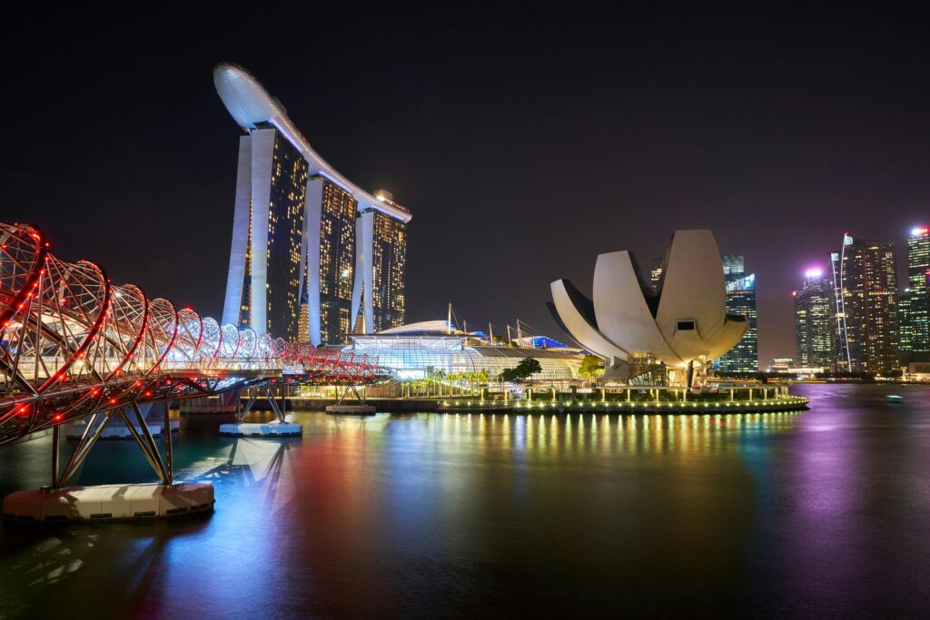 A stunning night view of the Singapore skyline featuring the iconic Marina Bay Sands, Helix Bridge, and ArtScience Museum, with vibrant lights reflecting on the water.