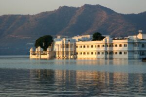 A stunning view of the Lake Palace in Udaipur, a white marble structure surrounded by calm waters, with mountains in the background under a soft evening sky.